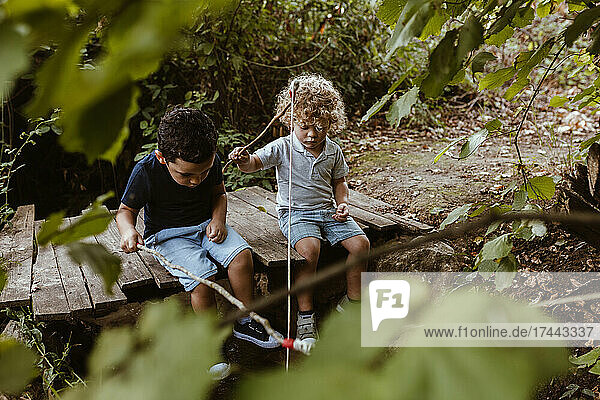 Curious boys fishing while sitting on footbridge