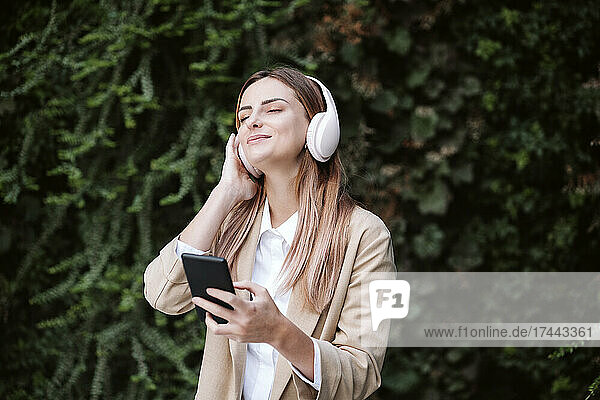 Female professional with eyes closed listening music through wireless headphones by plants