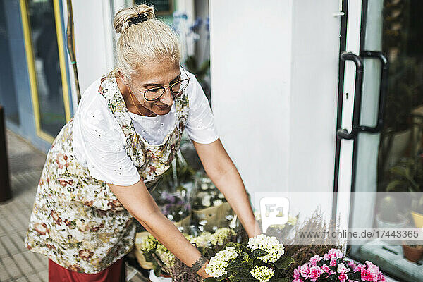 Blonde Floristin arrangiert Blumen vor dem Laden
