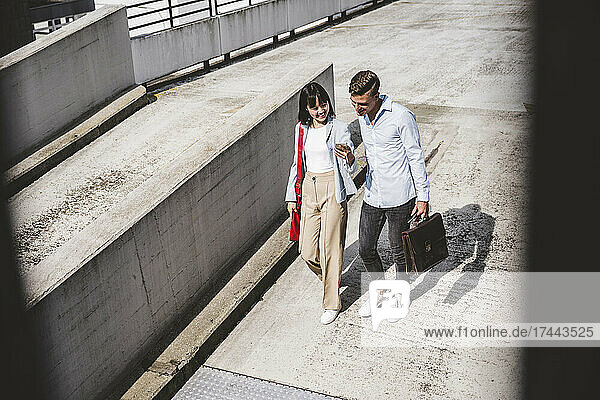 Male and female business professionals sharing mobile phone while walking on rooftop
