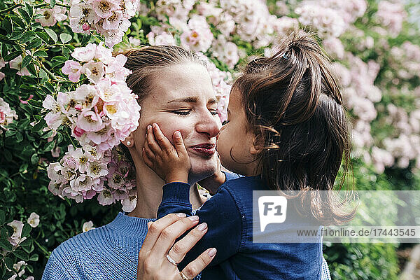 Daughter kissing mother by flowering plants