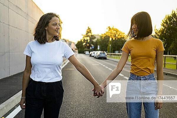 Young lesbian couple looking at each other while holding hands on road