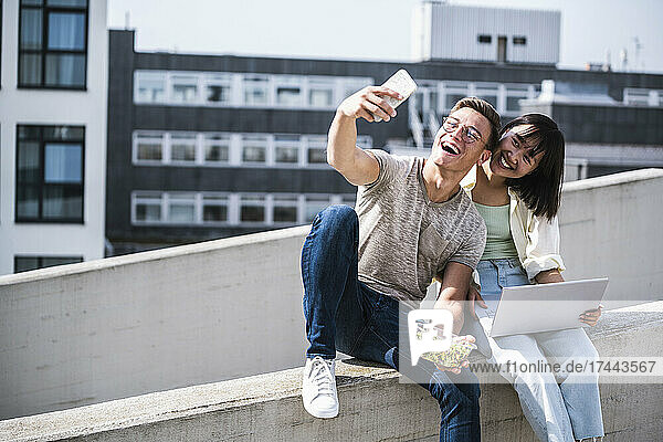 Happy male and female friends taking selfie through smart phone during sunny day