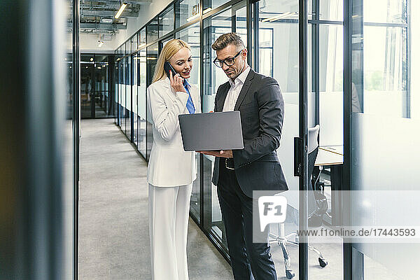 Businessman discussing with female colleague on laptop in corridor at office