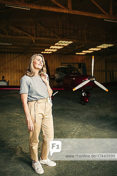 Smiling mature woman standing at airplane hangar