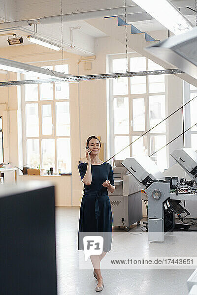 Businesswoman talking on mobile phone while walking in workshop