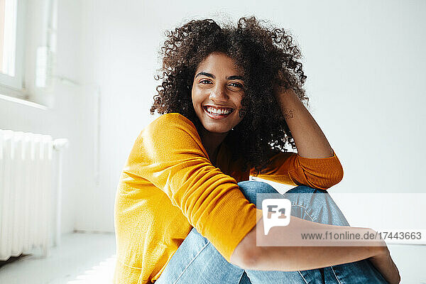 Smiling woman with hand in hair sitting on floor at home