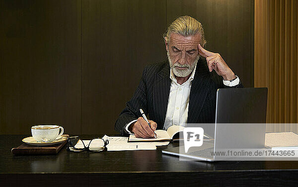 Businessman writing in diary while working at desk in hotel