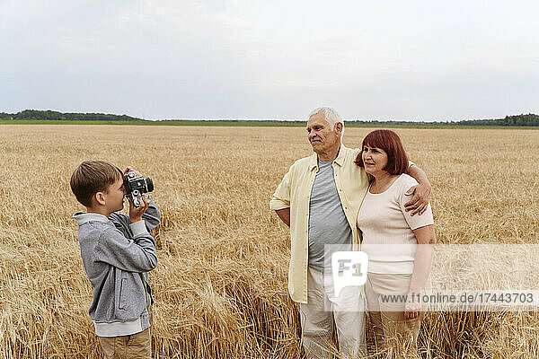 Grandson photographing grandparents through camera in wheat field
