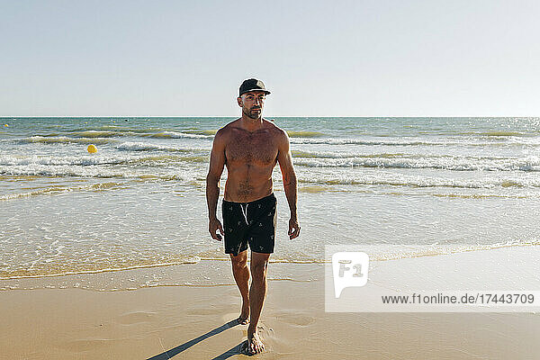 Shirtless man with cap walking on beach
