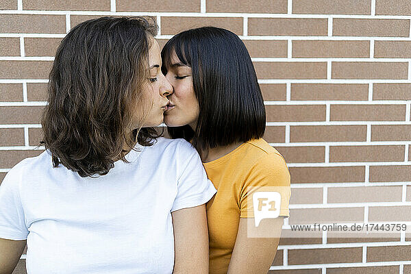 Affectionate lesbian couple kissing in front of brick wall