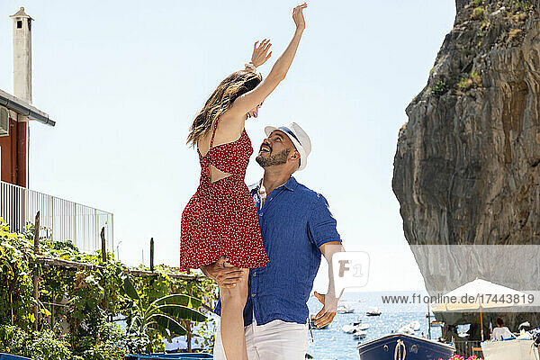 Happy man with panama hat lifting woman at beach