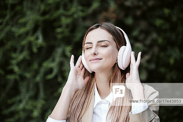 Lächelnde Geschäftsfrau mit geschlossenen Augen  die über kabellose Kopfhörer von Pflanzen Musik hört