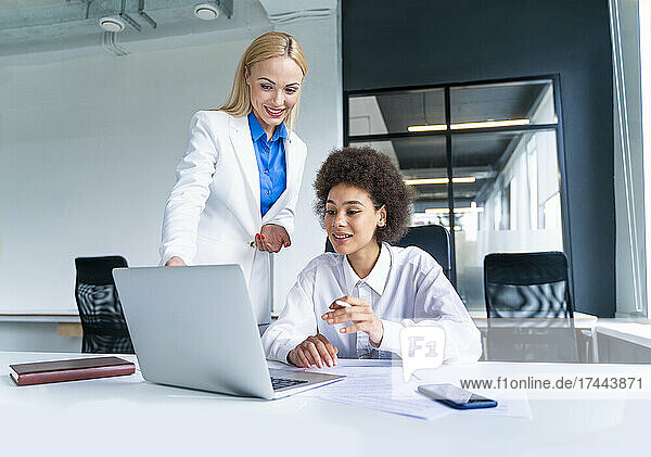 Smiling female business professionals discussing over laptop while working in office