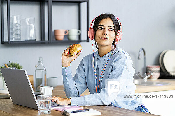 Beautiful woman with laptop having bun in kitchen