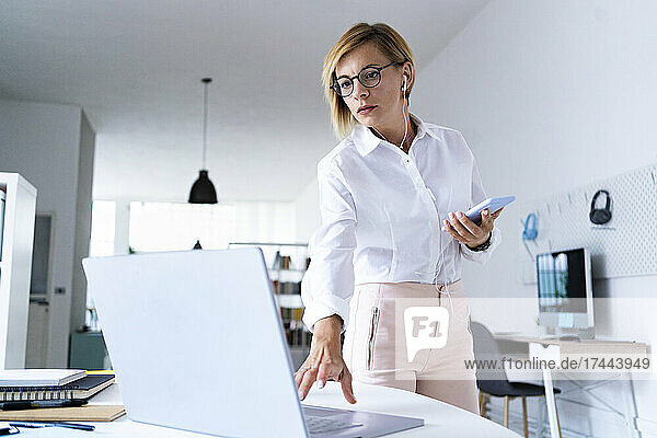 Female professional with mobile phone working on laptop at desk
