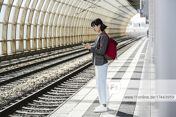 Teenage girl with backpack using mobile phone at train station