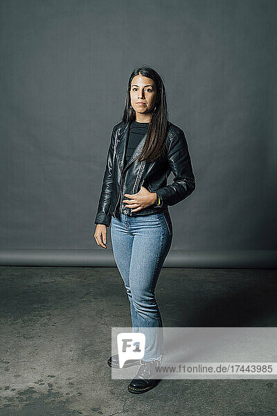 Young confident woman in leather jacket standing in studio