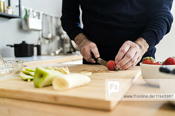 Senior man cutting strawberry on cutting board in kitchen