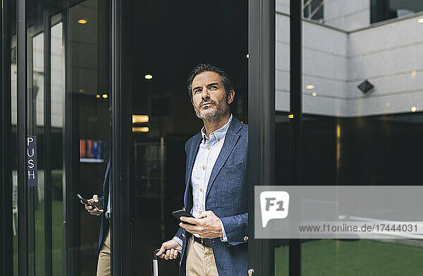 Mature businessman with mobile phone at doorway