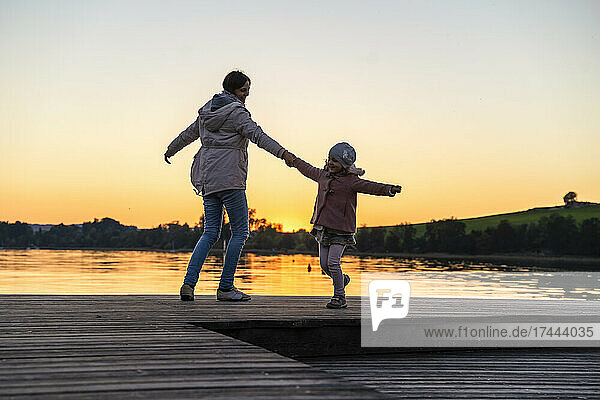 Mother and daughter dancing on pier during sunset
