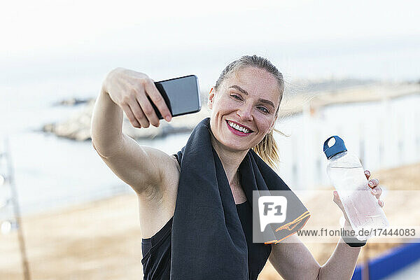 Sportswoman taking selfie through smart phone while holding water bottle