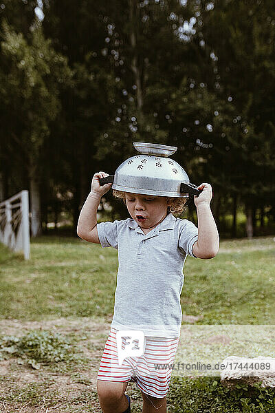 Boy wearing colander on head while playing on meadow