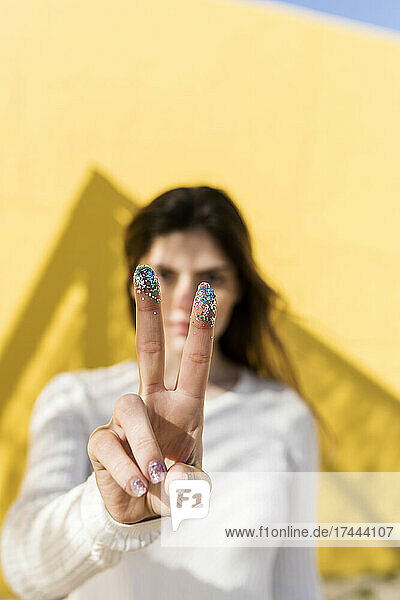 Frau gestikuliert mit Glitzer an den Fingern ein Friedenszeichen