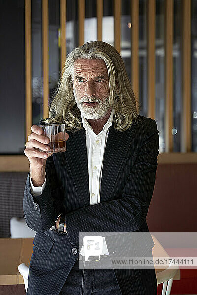 Male professional holding whiskey glass while standing at hotel cafe
