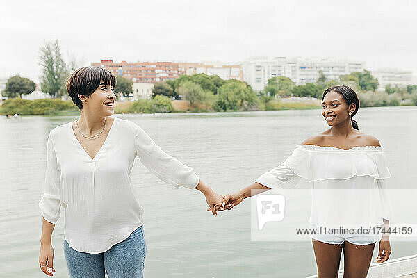 Lächelndes lesbisches Paar hält Händchen am Seeufer