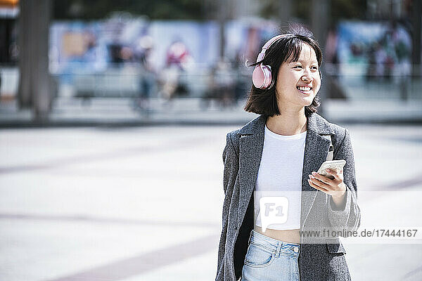 Happy teenage girl listening music through wireless headphones during sunny day
