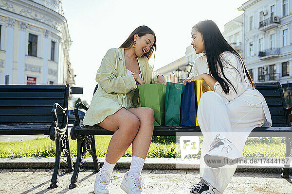 Happy female friends checking shopping bags on bench
