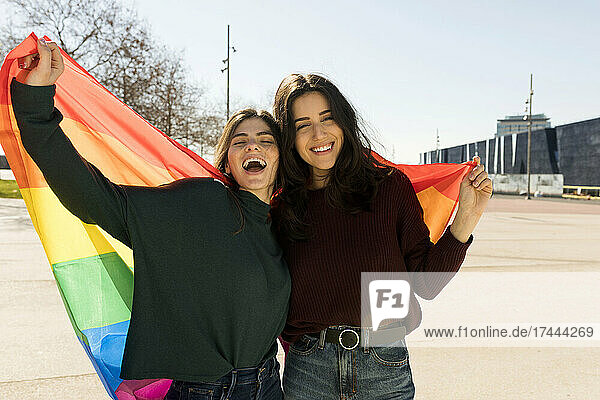 Glückliches lesbisches Paar hält an sonnigen Tagen eine Regenbogenfahne in der Hand