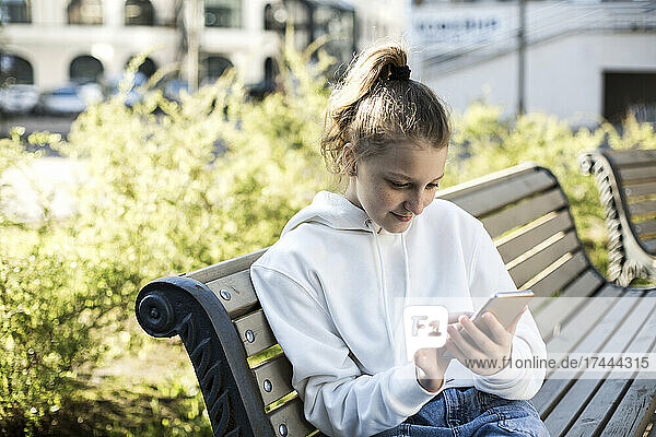 Girl using smart phone while sitting on bench
