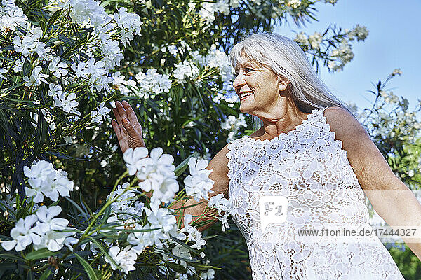 Smiling senior woman touching white flowers in park
