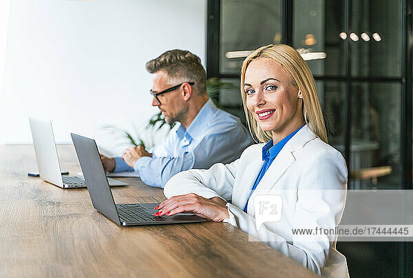 Smiling female professional sitting with male colleague at desk in office