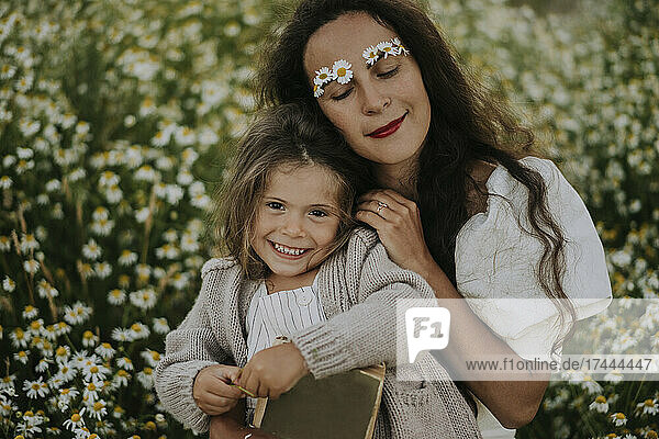 Mother leaning on smiling daughter at flower field