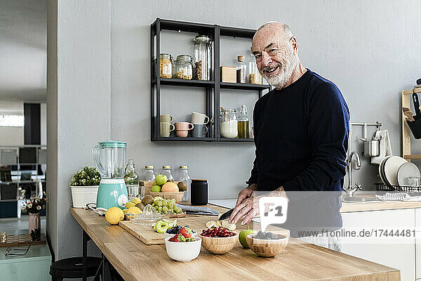 Smiling senior man cutting fruits in kitchen at home