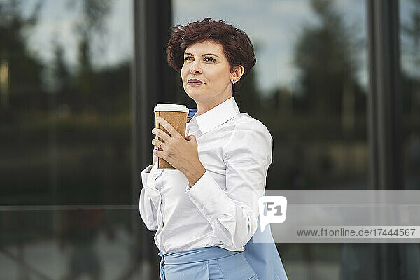 Female professional holding disposable cup while standing in front of glass wall