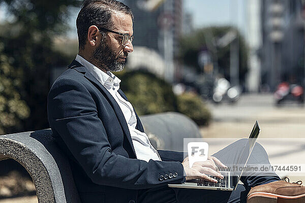 Männlicher Geschäftsprofi benutzt Laptop  während er auf der Bank sitzt