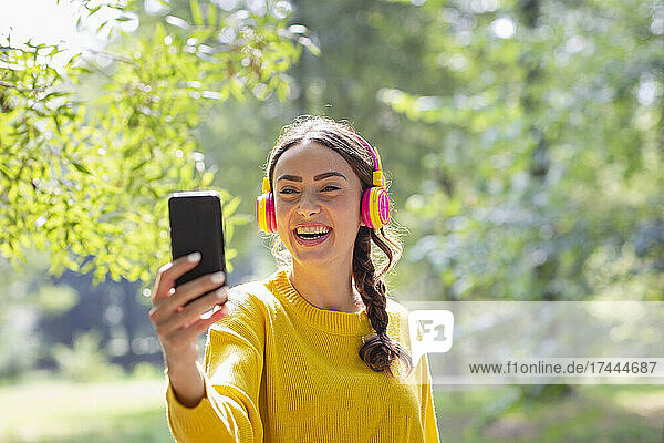 Happy woman with headphones taking selfie through smart phone at park