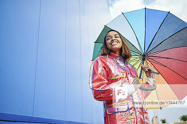 Young woman with multi colored umbrella in front of blue wall
