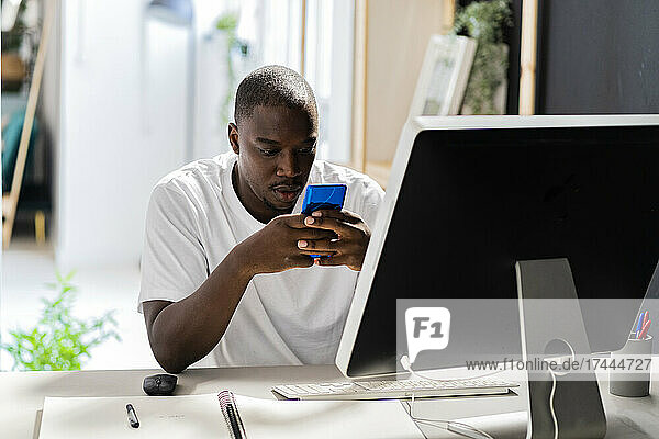 Male freelance worker using smart phone at desk in studio