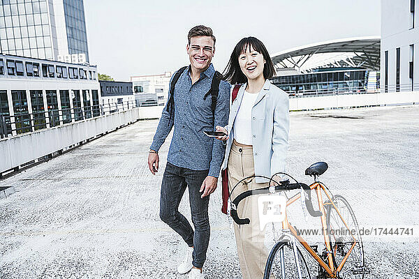 Happy male and female friends with bicycle walking on parking garage rooftop
