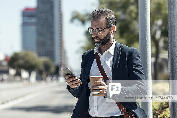 Männlicher Profi mit Einwegbecher und Mobiltelefon