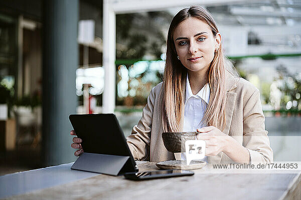 Geschäftsfrau mit digitalem Tablet und Kaffeetasse am Tisch sitzend