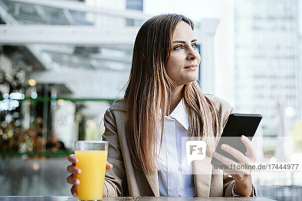 Female business professional with mobile phone and juice sitting at coffee shop