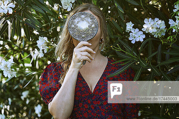 Woman holding mirror in front of flowering plant