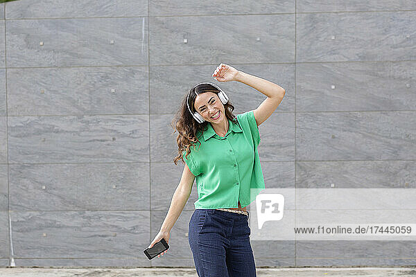 Carefree woman with wireless headphones dancing in front of wall