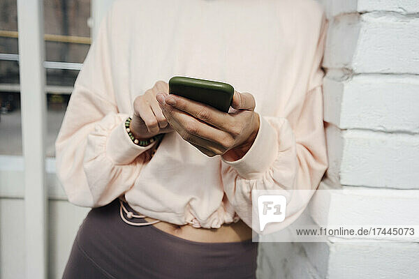Woman using smart phone while leaning on brick wall